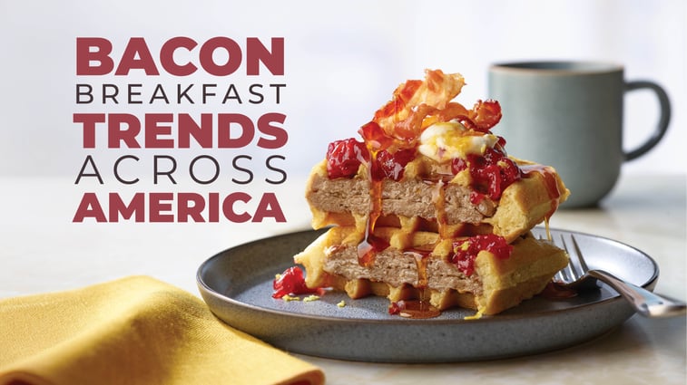 A stack of waffles topped with bacon, a sauce that looks like a berry compote, and a drizzle of syrup, on a dark plate. The text overlaid on the image reads "BACON BREAKFAST TRENDS ACROSS AMERICA". A dark gray mug is visible in the background.